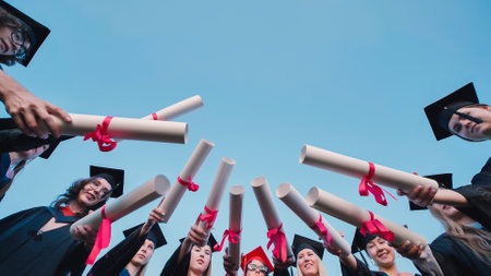 Graduates in caps and gowns joyfully raise their diplomas in celebration of their graduationの写真素材