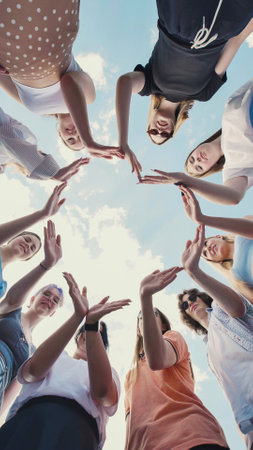Students demonstrating collaboration and friendship by forming a circle with their hands against a cloudy skyの写真素材