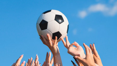 Many hands reaching for a soccer ball against a blue sky, symbolizing teamwork, sportsmanship, and school spiritの写真素材