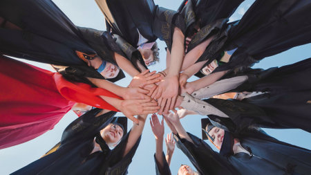Graduates joining hands in a circle from below, celebrating their success togetherの写真素材
