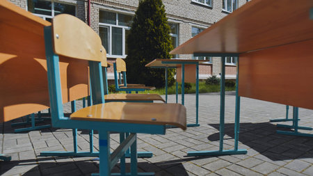 Empty desks and chairs stand outside a school building, suggesting an outdoor class or break time on...