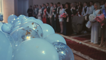 Blue balloons floating above scattered confetti, blurred graduates celebrating academic achievement...