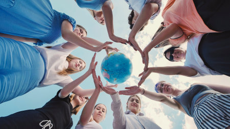 Group of school friends making a circle with their hands around a small globe, symbolizing environmental protection and global awarenessの写真素材