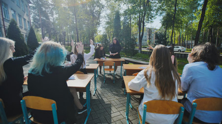 High school students raising hands to answer teachers question during open air lesson in schoolyardの写真素材