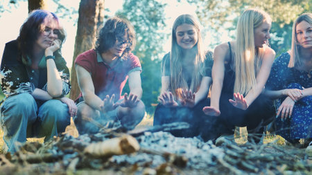 Students gathering around campfire, warming hands while sharing camaraderie during woodland eveningの写真素材