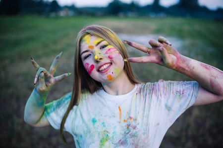 Joyful young woman with vibrant face paint and attire flashing a victory sign during the holi...