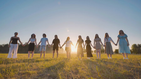 Young students linking hands in a field, savoring the summer sunset during a breakの写真素材