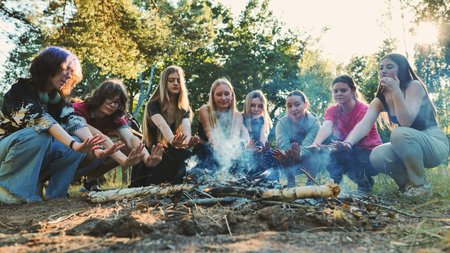 Group of teenage school friends warming their hands by bonfire during camping trip in forestの写真素材
