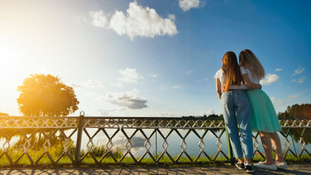 Teenage friends hugging near lakeside, watching golden sunset, sharing intimate connection amid serene natural landscapeの写真素材