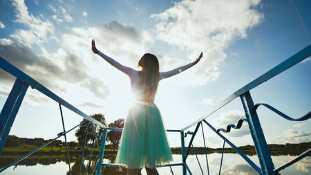 Young woman with open arms enjoying freedom on a bridge over a lake under a beautiful cloudy skyの写真素材