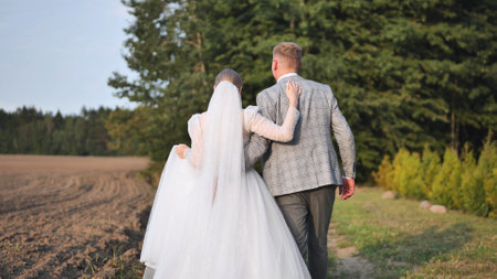 Newlyweds strolling hand in hand along woodland path, sharing intimate moment after wedding ceremonyの写真素材