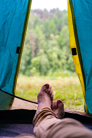 Legs and bare feet of a camper relaxing inside a tent, enjoying the peaceful view of a green forestの写真素材