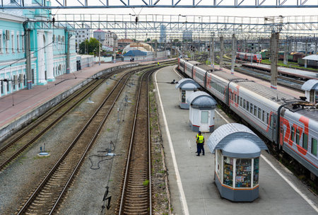 Train leaving station platform with railway workers supervising operations and small shops on the...