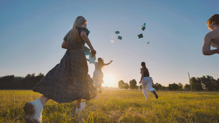 Group of high school students running in a field throwing their notebooks in the air celebrating the end of school yearの写真素材