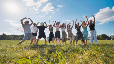 High school students celebrating their summer break by jumping with arms raised in a green field, expressing joy and freedomの写真素材