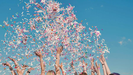 Students throwing confetti in the air during graduation ceremony celebrating their academic achievement under blue skyの写真素材