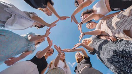 High school students unite in a circle with their hands against a blue sky, showcasing teamwork and friendship during summer vacationの写真素材