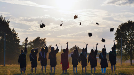 Group of students in academic gowns joyfully throwing graduation caps into the air during a vibrant sunset, celebrating their achievements togetherの写真素材