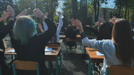 Happy students raising their hands at outdoor desks, celebrating the end of the school dayの写真素材