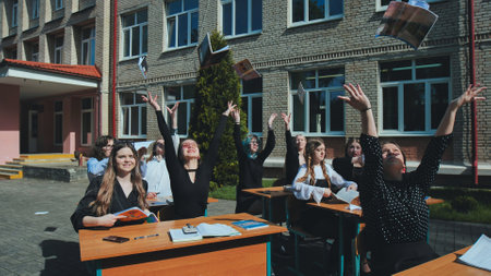 Cheerful students throwing books in the air to celebrate the end of the school year outside the school buildingの写真素材