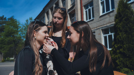 Three teenagers are putting on makeup while taking a break, enjoying the sunshine outside their high schoolの写真素材