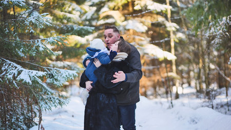 Winter forest setting with cheerful parents cuddling, playing with infant, enjoying serene snowy landscape togetherの写真素材