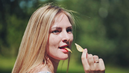 Blonde woman enjoying crispy potato chip, basking in summer sunlight, embodying casual snacking...