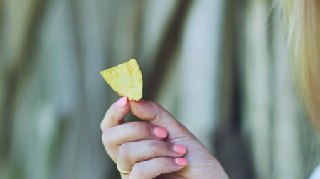Well groomed female hand grasping single golden potato chip, anticipating savory crisp snacking experienceの写真素材