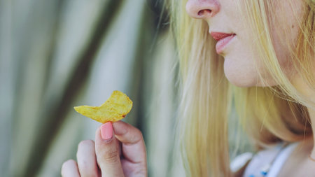 Blond woman gripping potato chip near mouth, preparing to bite crispy snackの写真素材