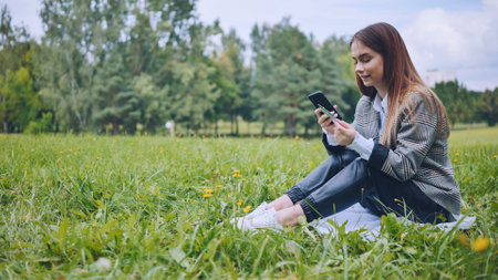Businesswoman making online payment using credit card and smartphone while sitting on grass in a parkの写真素材
