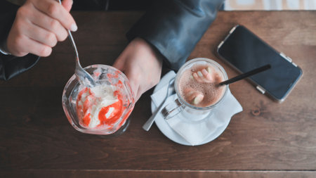 Person savoring sweet treats, smartphone beside coffee mug at cozy cafe settingの写真素材