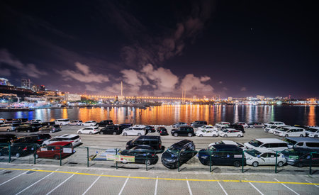 Night scene featuring illuminated bridge, parked vehicles, cityscapeの写真素材