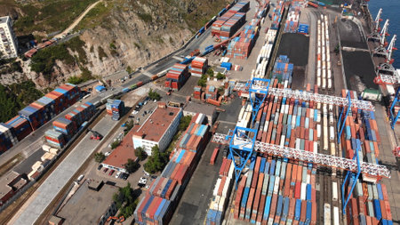 Industrial cargo port with cranes loading colorful shipping containers onto train cars, aerial view of global logistics and transportation hubの写真素材