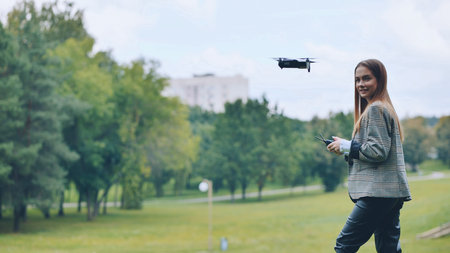 A cute girl controls a drone in the park.