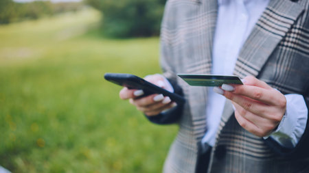 A young business lady makes a purchase with her phone and bank card in the park.