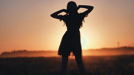 A silhouette of a young girl dancing and spinning on a warm summer evening at sunset.の写真素材