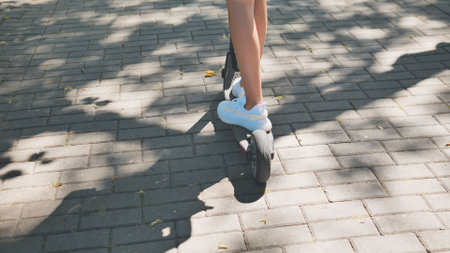 Young woman gliding electric scooter through urban green space, experiencing leisurely summer mobilityの写真素材