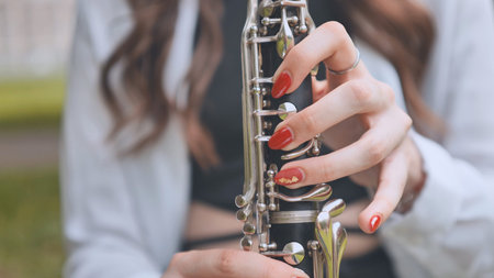 Skilled musician performing clarinet, sunlit outdoor setting revealing precise finger placement and...