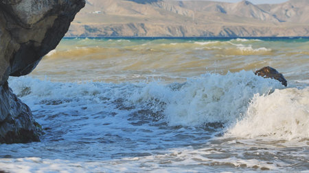 Powerful waves striking rocky crimean shoreline, mountainous terrain rising behind azure waters