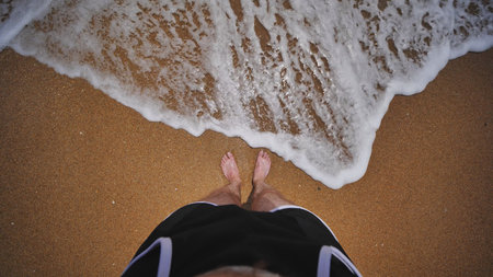 Tourist standing on Crimean beach enjoying foamy wave washing his feetの写真素材