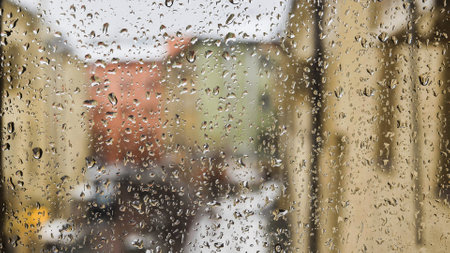 Raindrops sliding on window glass blurring cityscape viewの写真素材