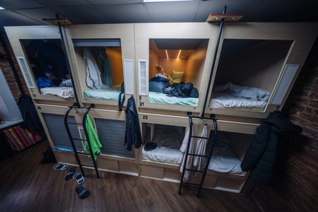 Capsule hotel beds showing clothes and bags hanging, offering affordable accommodationの写真素材