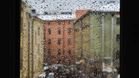Raindrops sliding on window glass blurring buildings in the backgroundの写真素材