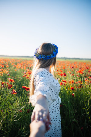 Romantic couple holding hands while walking through a vibrant poppy field, enjoying a peaceful summer day togetherの写真素材