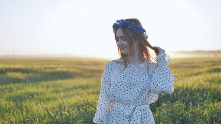Young woman wearing flower crown, standing in verdant meadow during golden hour, experiencing serene natural landscapeの写真素材