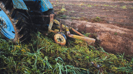 Old blue tractor plowing the soil in an agricultural field, preparing for sowing, creating furrows in the fertile landの写真素材