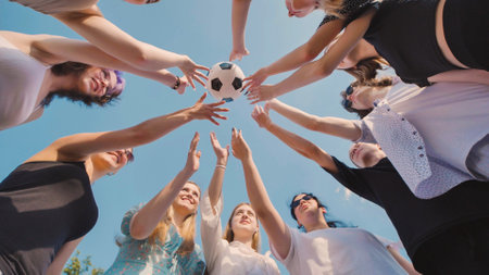 High school students showing unity and teamwork as they reach for a soccer ball under the summer sky, symbolizing friendship and love for the sportの写真素材