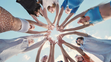 School friends joining hands in a circle, showing teamwork and unity under a bright skyの写真素材