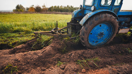 Vintage blue tractor plowing autumn field, creating deep furrows across fertile farmland landscapeの写真素材