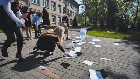 Students joyfully celebrating the end of their exams by throwing papers in the air and enjoying...